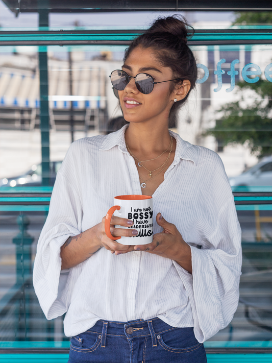 A woman holding an orange ceramic mug with the text 'not bossy, just born to lead!' on it, smiling and standing near a window.