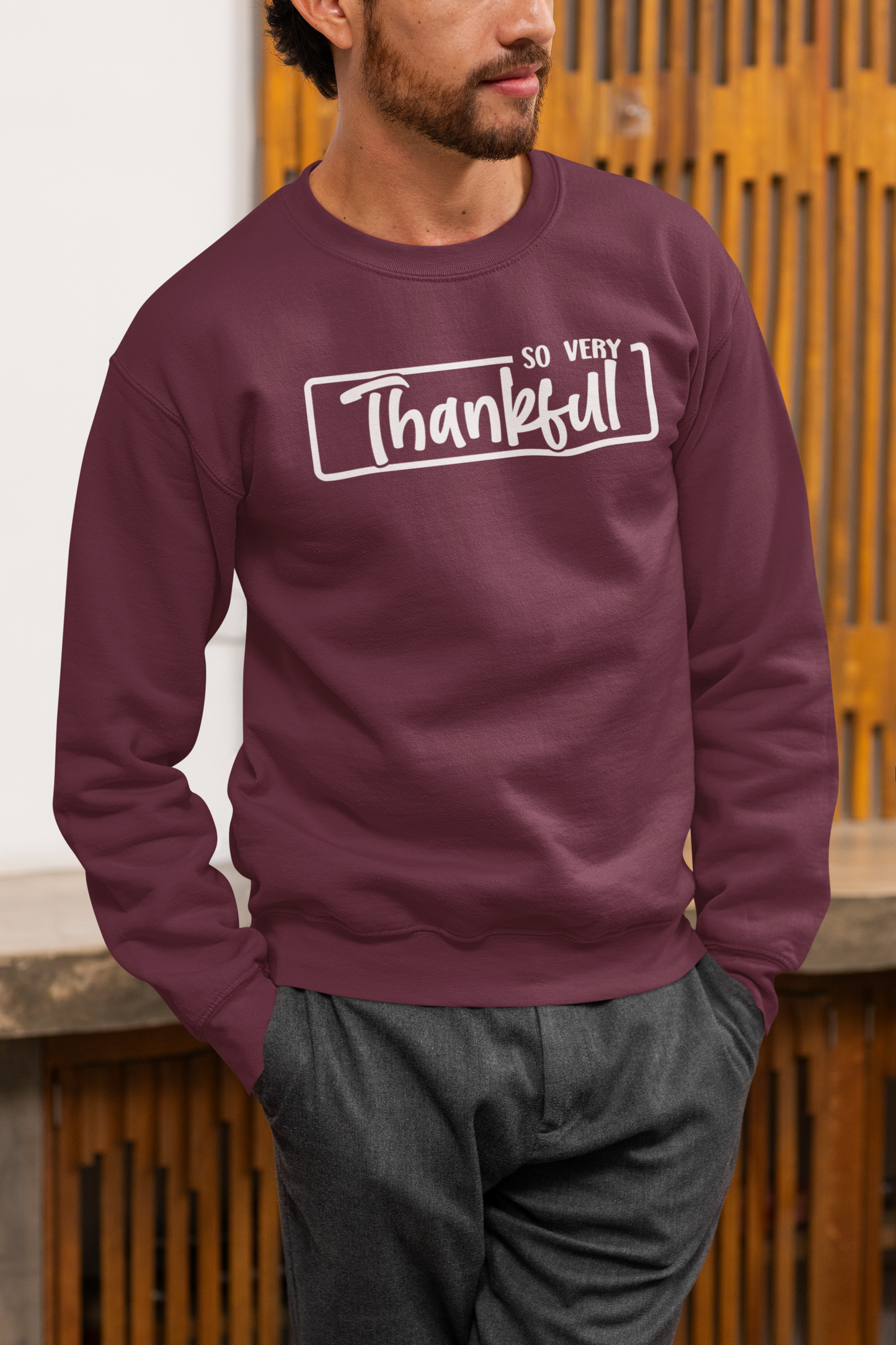 Person wearing a maroon sweatshirt with 'So Very Thankful' text against a wooden background
