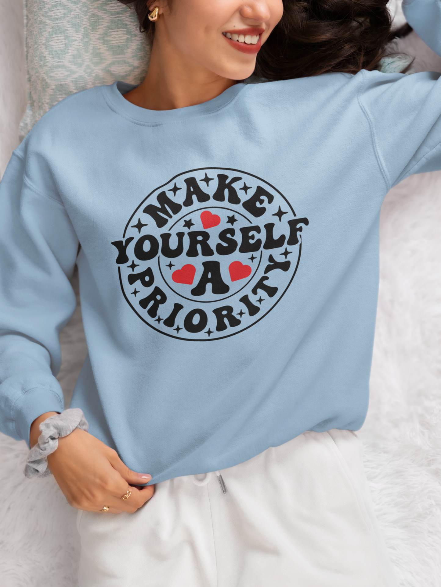A person wearing a light blue unisex sweatshirt with the text 'MAKE YOURSELF A PRIORITY' printed on the front.