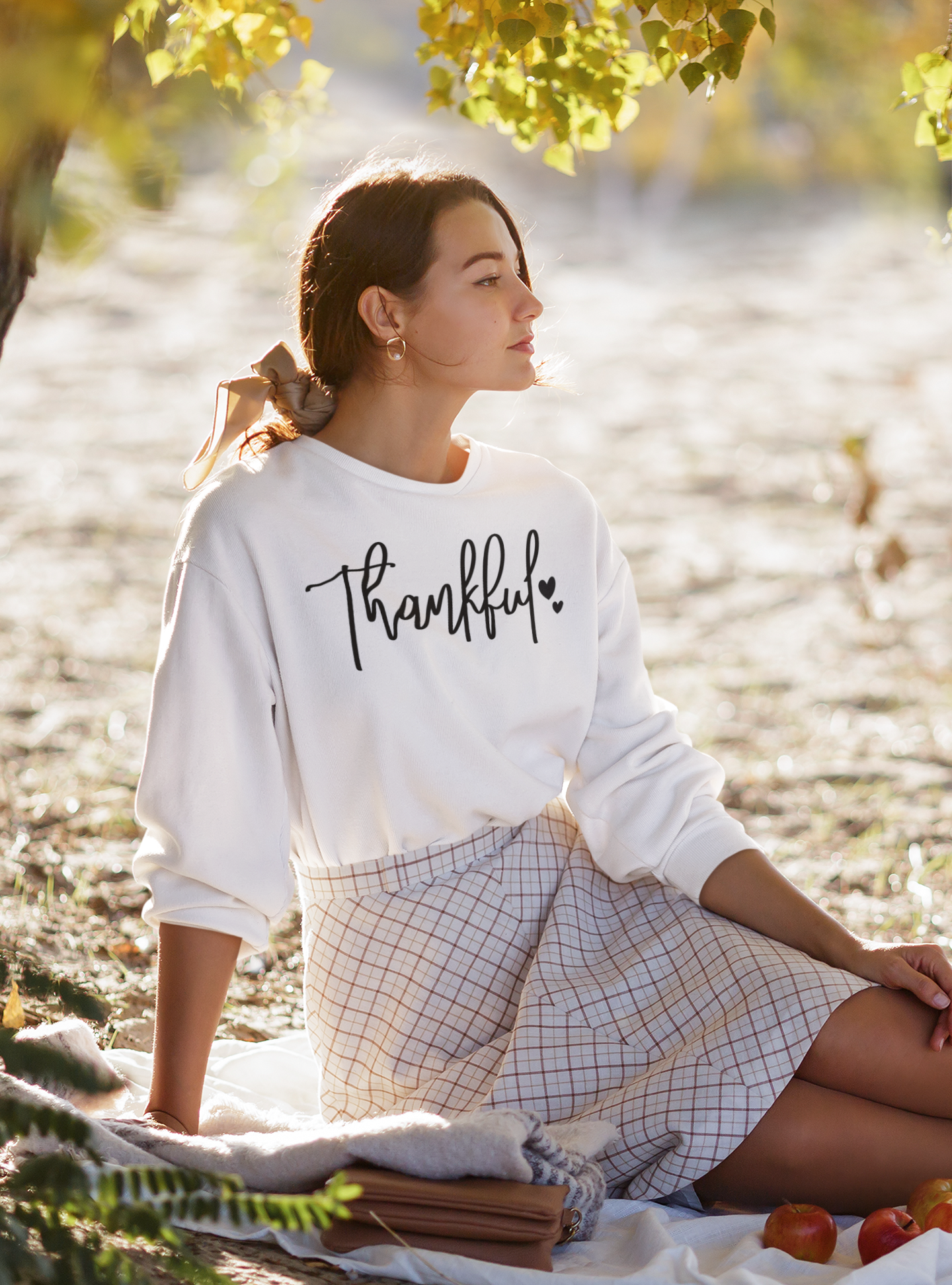 Woman sitting by a lake wearing a 'Thankful' shirt, surrounded by nature.
